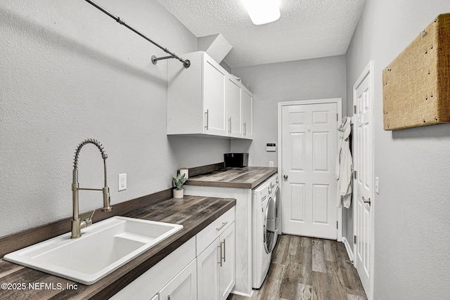 washroom featuring wood finished floors, washer and clothes dryer, a textured ceiling, a sink, and cabinet space