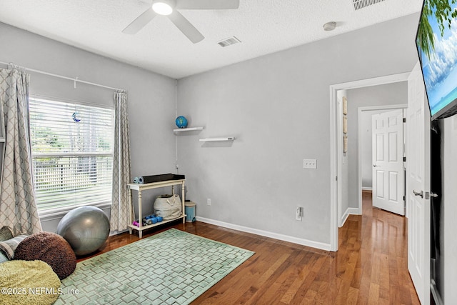 interior space featuring a textured ceiling, a ceiling fan, baseboards, wood finished floors, and visible vents