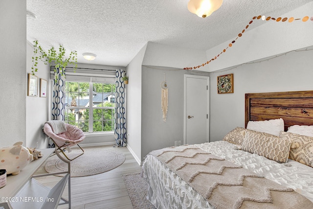 bedroom featuring light wood-style floors, baseboards, and a textured ceiling