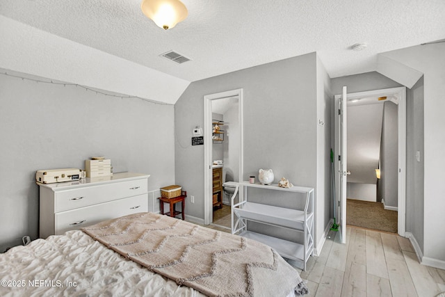 bedroom featuring a textured ceiling, baseboards, vaulted ceiling, light wood-type flooring, and visible vents