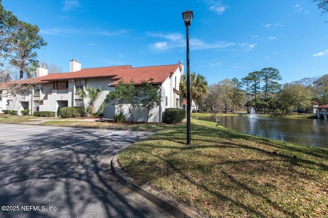 view of front of house featuring a chimney, uncovered parking, a front lawn, stucco siding, and a water view