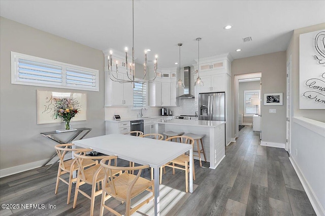 kitchen with light countertops, glass insert cabinets, appliances with stainless steel finishes, white cabinetry, and wall chimney range hood