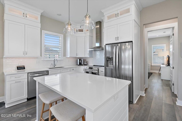 kitchen with a center island, stainless steel appliances, white cabinetry, a sink, and wall chimney exhaust hood