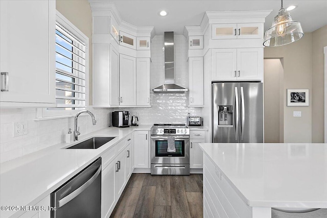 kitchen featuring stainless steel appliances, light countertops, wall chimney range hood, pendant lighting, and a sink