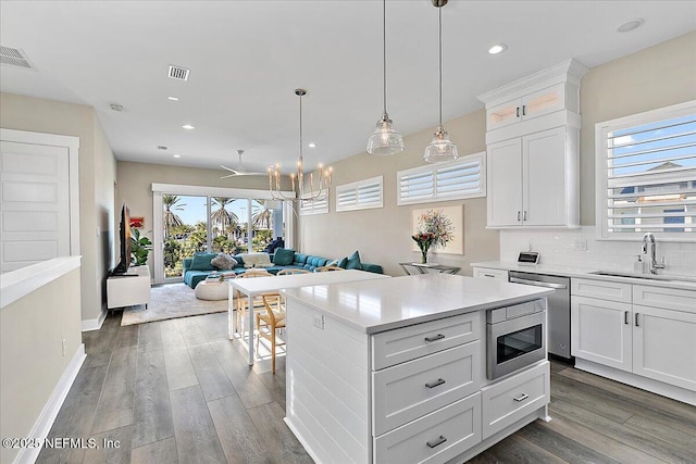 kitchen with open floor plan, light countertops, white cabinetry, pendant lighting, and a sink