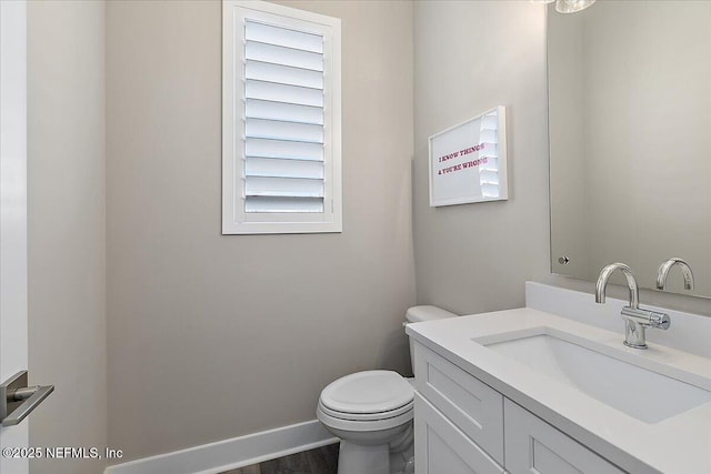 half bathroom with toilet, baseboards, and vanity