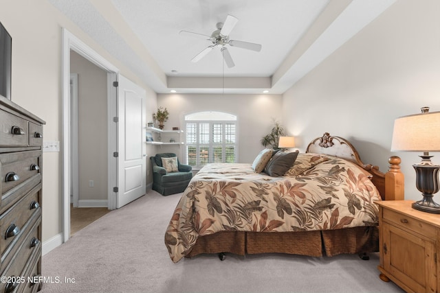 bedroom with baseboards, a raised ceiling, a ceiling fan, and light colored carpet