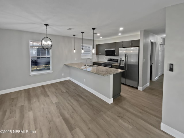 kitchen with pendant lighting, sink, kitchen peninsula, stainless steel appliances, and light stone countertops