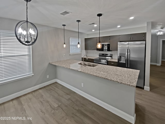 kitchen with pendant lighting, sink, stainless steel appliances, light stone counters, and kitchen peninsula