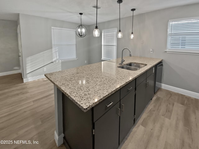 kitchen featuring decorative light fixtures, dishwasher, sink, light stone counters, and light hardwood / wood-style flooring