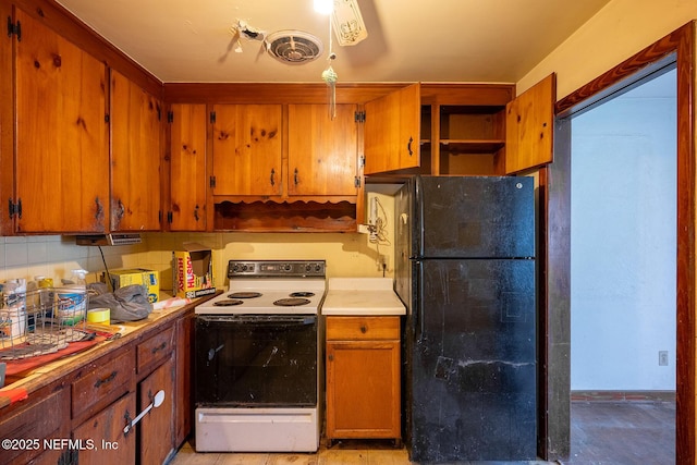 kitchen with white electric stove, tasteful backsplash, and black refrigerator