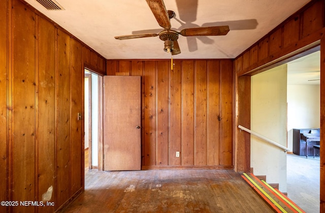 unfurnished room with ceiling fan, wooden walls, and hardwood / wood-style floors