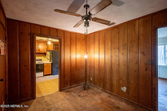 unfurnished room with ceiling fan, wooden walls, and light hardwood / wood-style floors