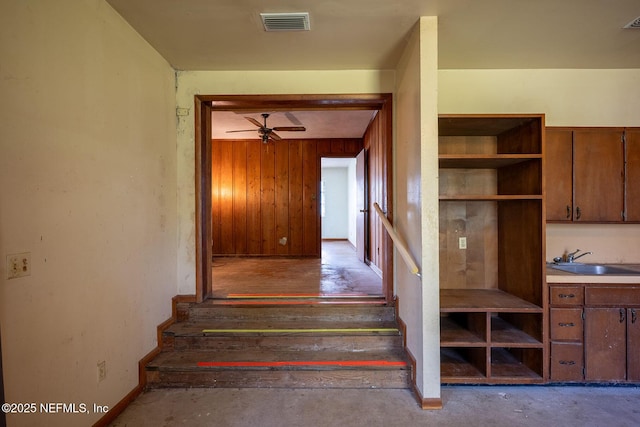 staircase with ceiling fan, wooden walls, sink, and concrete floors