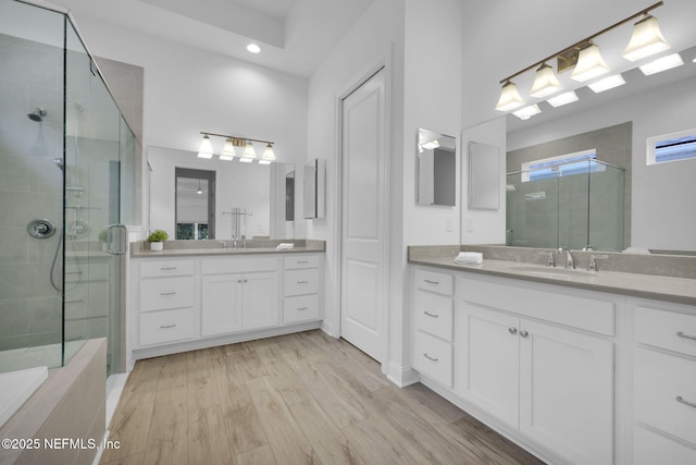 bathroom with a shower stall, two vanities, a sink, and wood finished floors