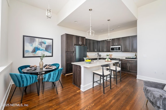 kitchen featuring dark brown cabinetry, stainless steel appliances, decorative light fixtures, and a center island with sink