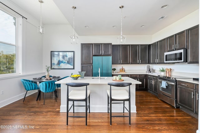 kitchen featuring stainless steel range with electric stovetop, a kitchen bar, decorative light fixtures, and a kitchen island with sink