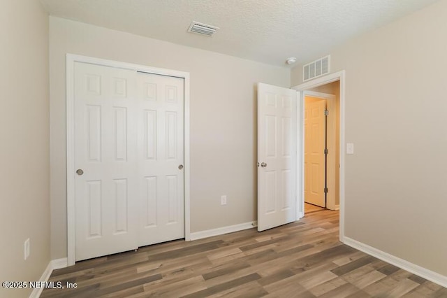 unfurnished bedroom featuring hardwood / wood-style flooring, a closet, and a textured ceiling