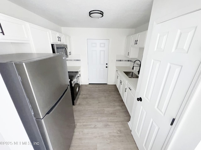 kitchen featuring appliances with stainless steel finishes, sink, white cabinets, and light hardwood / wood-style flooring