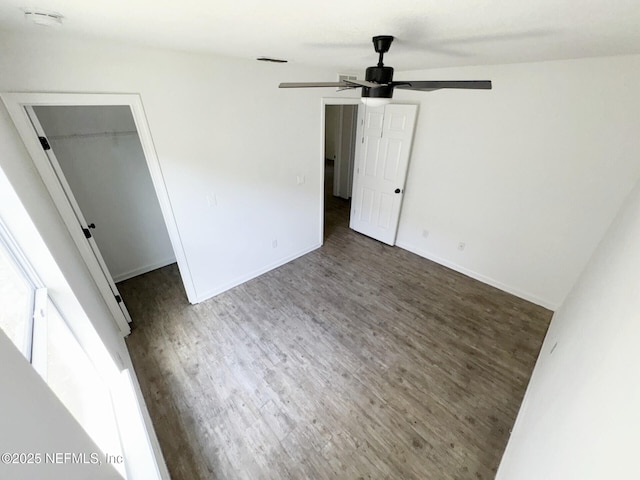 unfurnished bedroom featuring a spacious closet, dark wood-type flooring, a closet, and ceiling fan