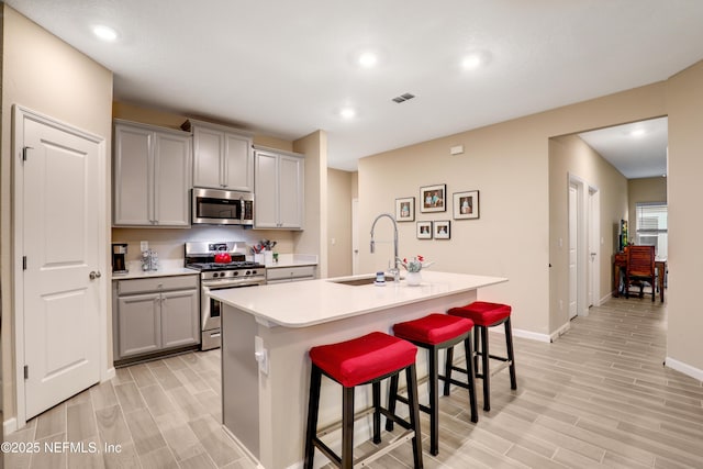 kitchen featuring a center island with sink, a kitchen bar, appliances with stainless steel finishes, and gray cabinets