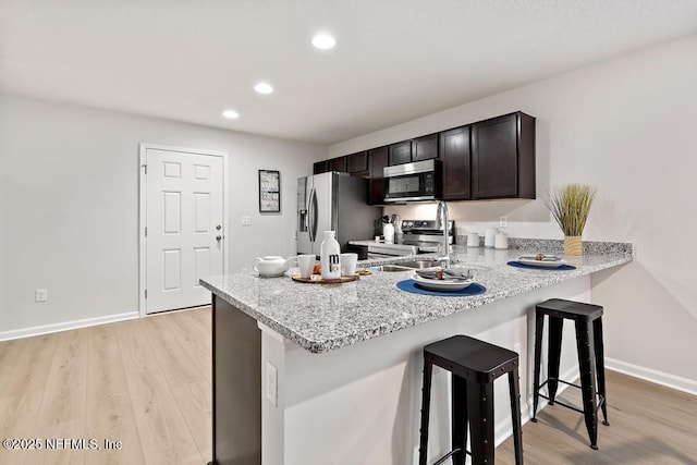 kitchen featuring dark brown cabinetry, light hardwood / wood-style flooring, a kitchen breakfast bar, kitchen peninsula, and stainless steel appliances