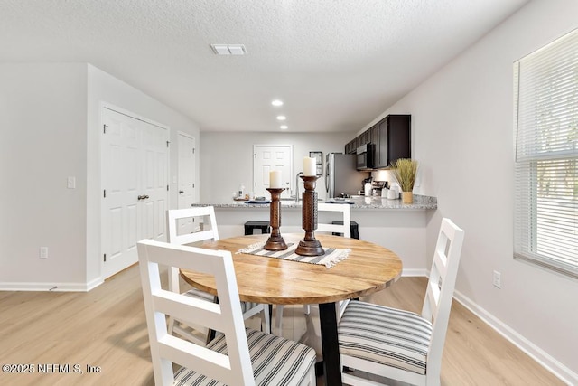 dining space with a textured ceiling and light hardwood / wood-style floors