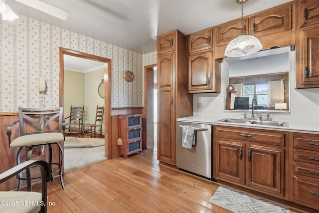 kitchen with sink, hanging light fixtures, stainless steel dishwasher, crown molding, and light wood-type flooring