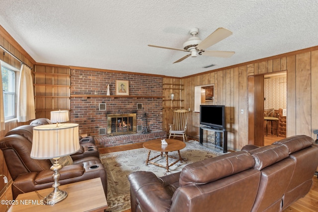 living room with crown molding, wooden walls, a fireplace, light hardwood / wood-style floors, and a textured ceiling