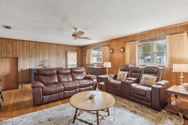 living room with crown molding, ceiling fan, light hardwood / wood-style floors, a textured ceiling, and wood walls