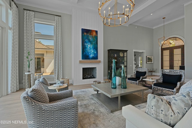 living room with a high ceiling, an inviting chandelier, a fireplace, crown molding, and wood finished floors