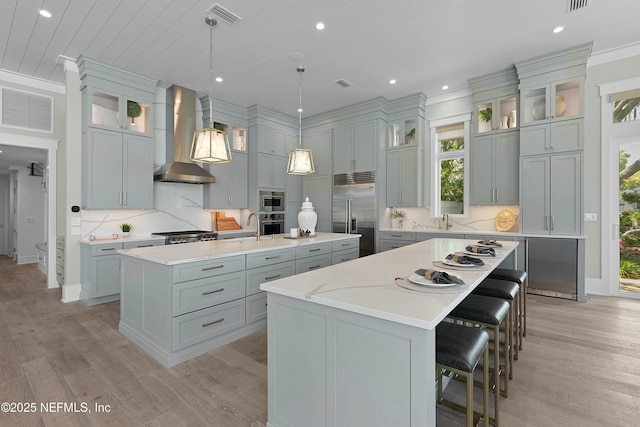 kitchen featuring a spacious island, wall chimney exhaust hood, visible vents, and stainless steel appliances