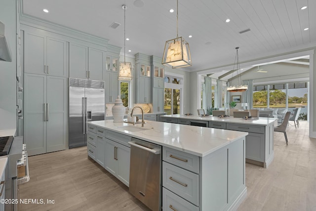 kitchen with gray cabinets, a sink, stainless steel appliances, a center island with sink, and light wood finished floors