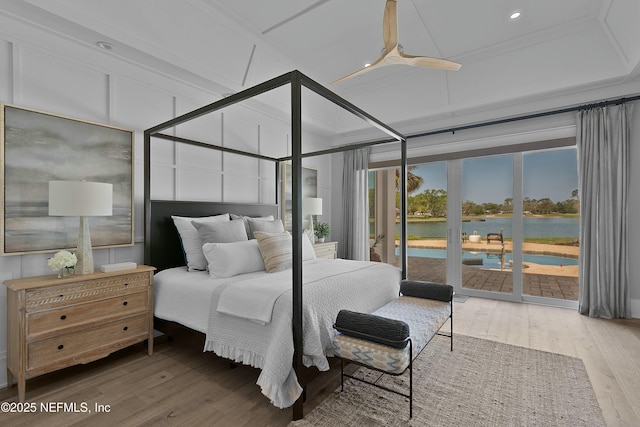 bedroom with a decorative wall, access to outside, a water view, and wood finished floors