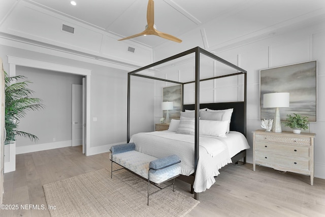 bedroom with a decorative wall, light wood-style flooring, a ceiling fan, visible vents, and baseboards