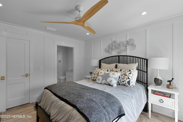 bedroom with a decorative wall, ensuite bathroom, a ceiling fan, and wood finished floors