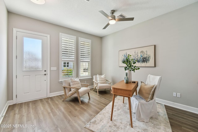 sitting room with ceiling fan, a textured ceiling, baseboards, and wood finished floors