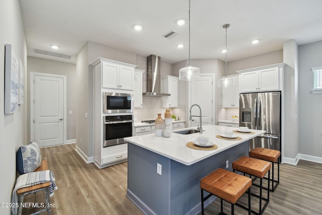 kitchen with visible vents, appliances with stainless steel finishes, white cabinets, wall chimney exhaust hood, and a sink