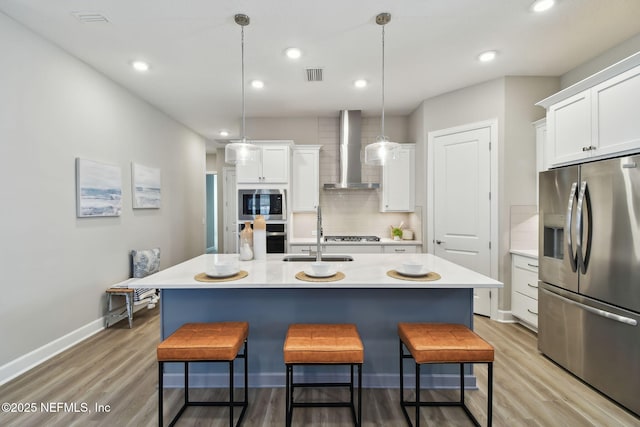 kitchen with visible vents, a sink, backsplash, stainless steel appliances, and wall chimney range hood