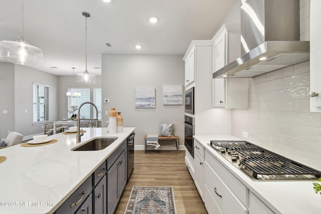 kitchen featuring a sink, wood finished floors, white cabinetry, stainless steel appliances, and wall chimney range hood