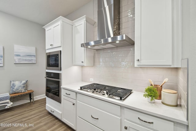 kitchen featuring wood finished floors, stainless steel appliances, light countertops, white cabinetry, and wall chimney exhaust hood