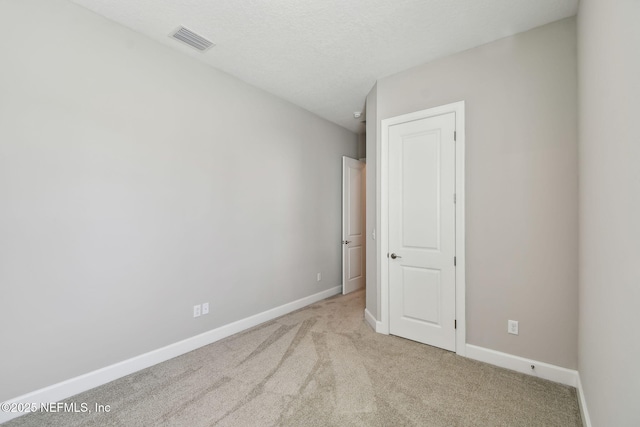 unfurnished room featuring a textured ceiling, light colored carpet, visible vents, and baseboards