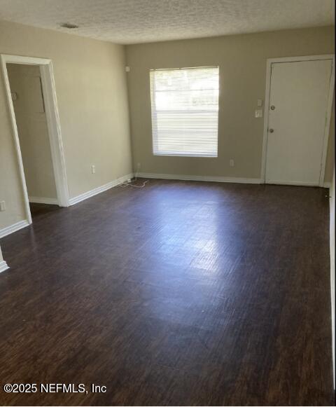 unfurnished room with dark wood-style flooring, a textured ceiling, and baseboards