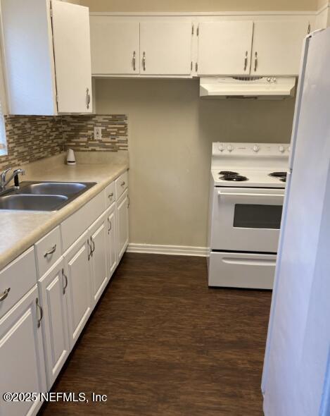 kitchen with white appliances, white cabinets, backsplash, under cabinet range hood, and a sink