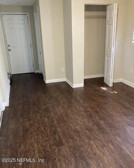 unfurnished bedroom with a closet, baseboards, and dark wood-style flooring