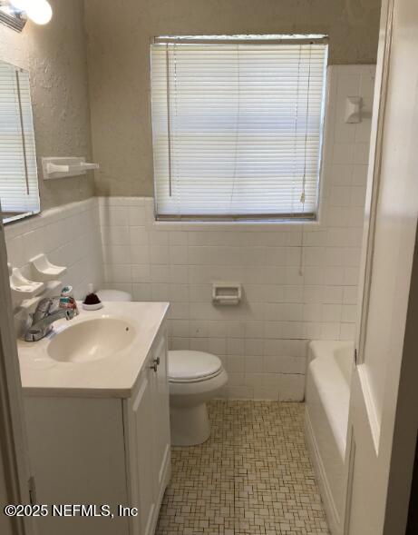 bathroom with a washtub, tile walls, toilet, vanity, and walk in shower