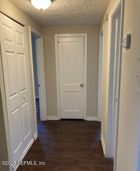 corridor featuring a textured ceiling, baseboards, and dark wood-style flooring