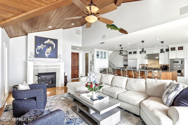 living area featuring visible vents, lofted ceiling with beams, a tiled fireplace, wood finished floors, and wooden ceiling