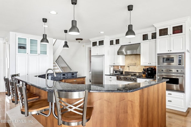 kitchen featuring built in appliances, under cabinet range hood, a breakfast bar, a spacious island, and decorative backsplash