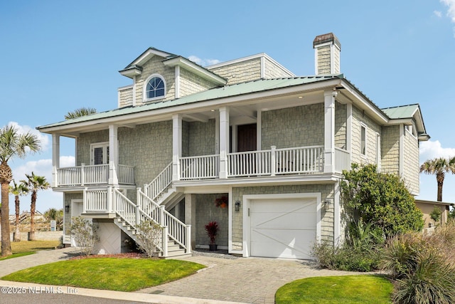 view of front of property with stairway, metal roof, an attached garage, decorative driveway, and a porch